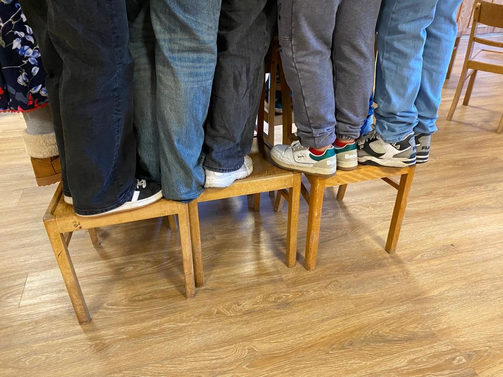 Gruppenübung bei "Wir sind stark": Die Schüler*innen stehen gemeinsam auf wenigen Stühlen und müssen sich gegenseitig halten.